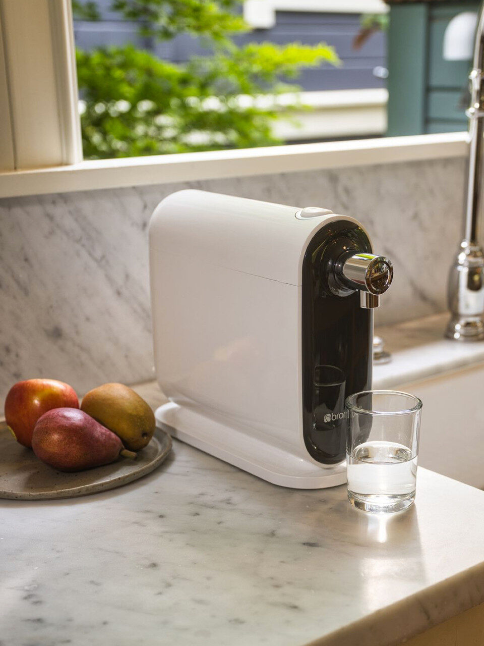 The Brondell Cyprus Three Stage Countertop Water Filtration System set on a kitchen counter with a glass half full of water in front of it.