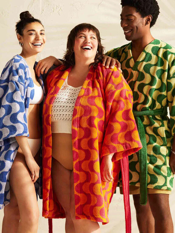 Three models wearing Brooklinen's Wavelength robe in blue, orange and green.