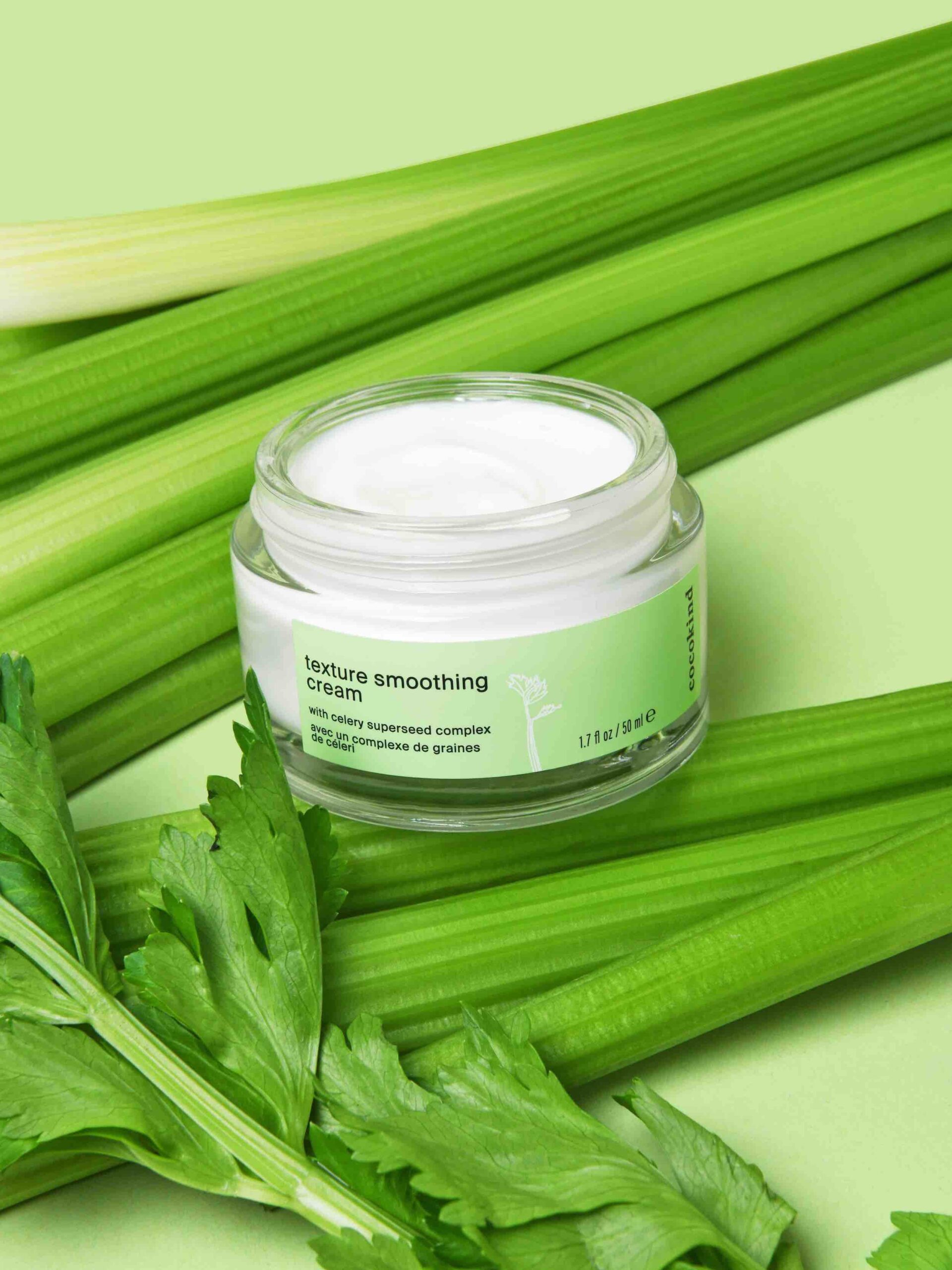 An open glass jar of cocokind's texture smoothing cream with celery in the background.