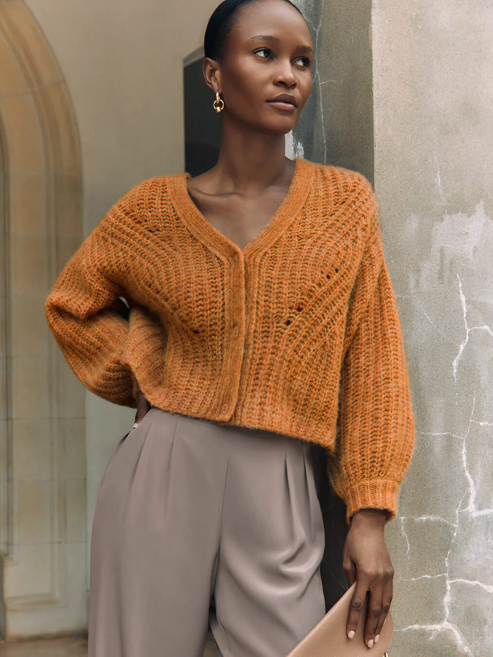 A model wearing a burnt orange crop cardigan by Cuyana.