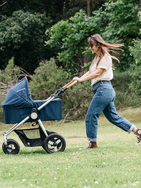 A woman pushing a dark blue baby carrier across the grass. By Earth Hero.