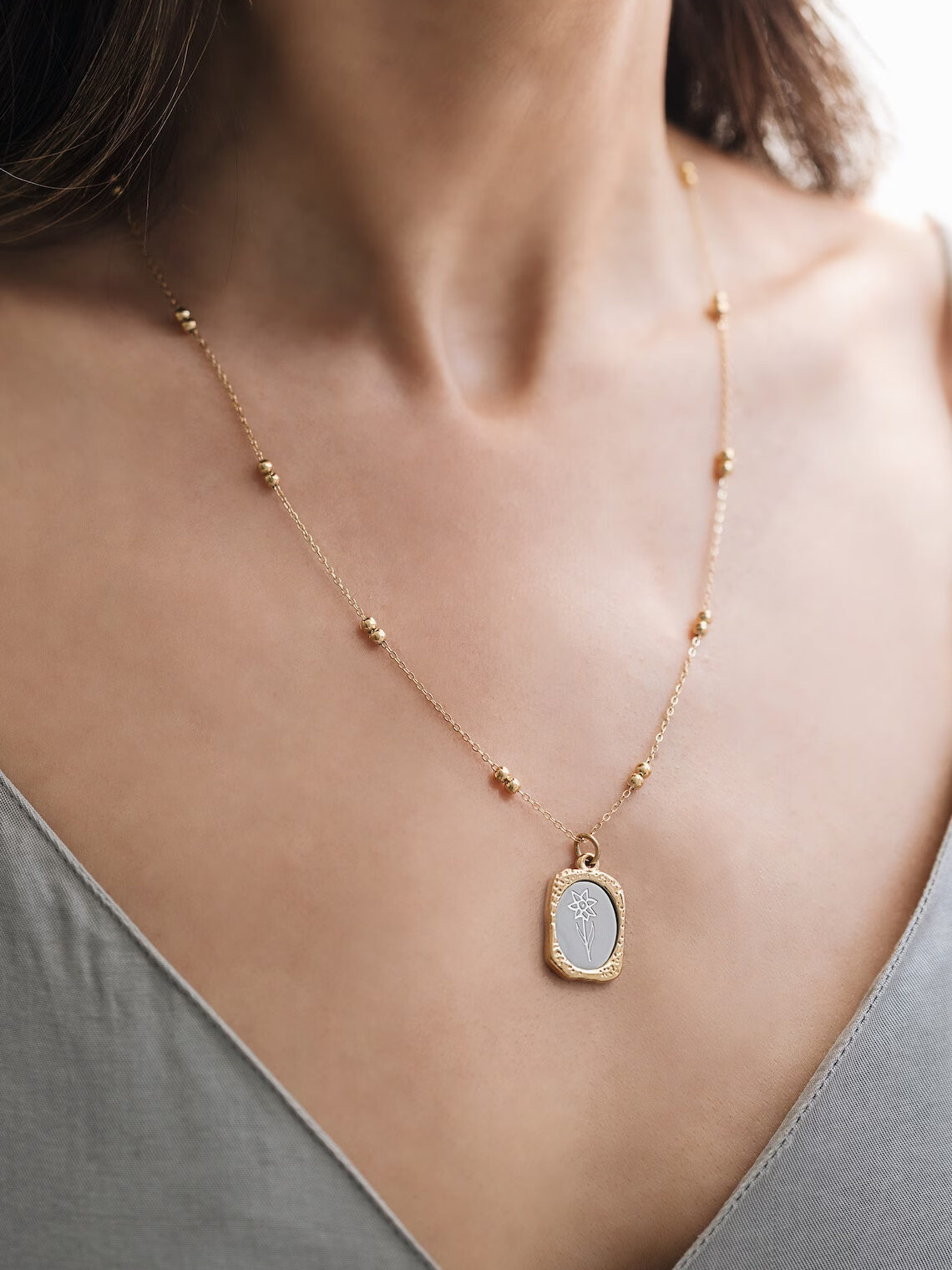 A model wearing a yellow gold pendant necklace in the shape of a rounded rectangle with a mirror in the center containing a flower engraving. Found on Etsy. 