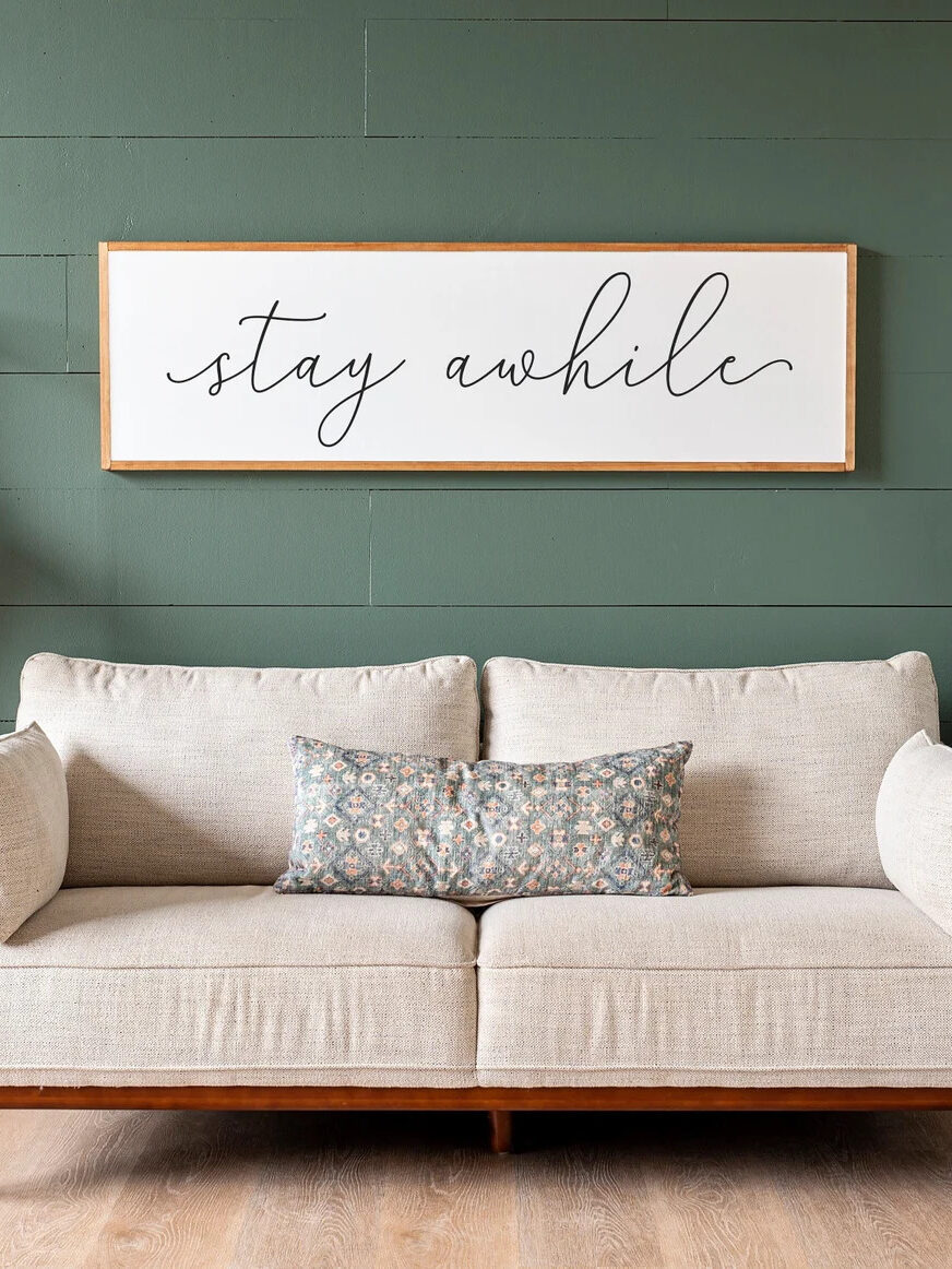 A rectangular frame with the words "stay awhile", written in cursive. The frame is on a teal-green wall. 