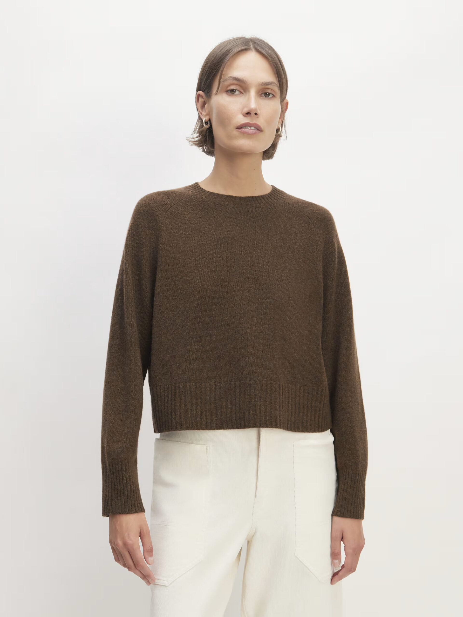 A model wearing a brown boxy knit sweater by Everlane.