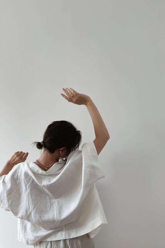 Woman with hands up standing against white wall. Minimal fashion concept.