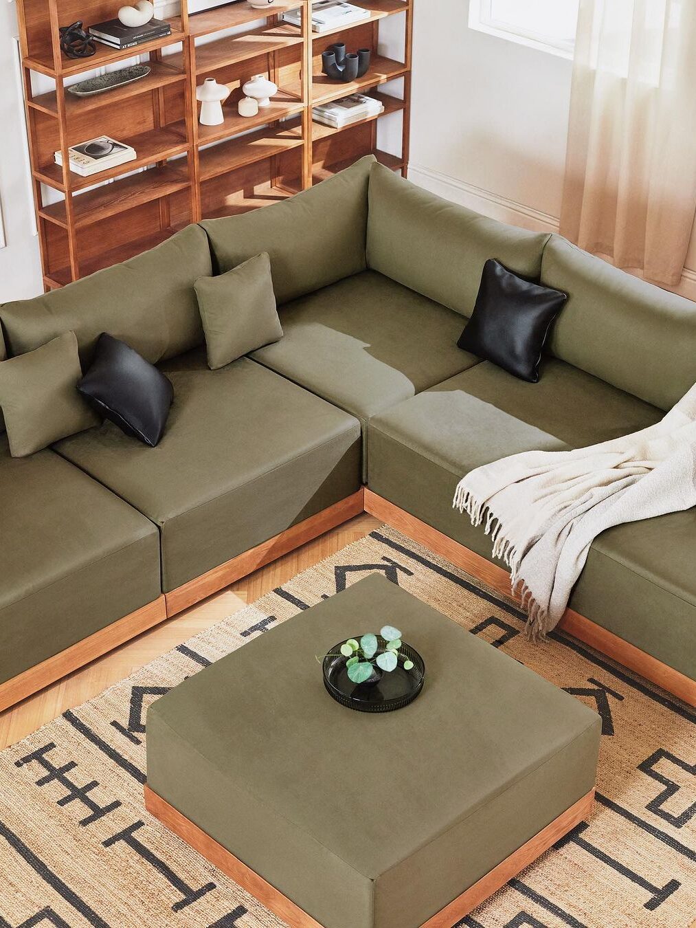 A sage green Inside Weather modular couch with matching green pillow and black leather pillows in a living room setting.