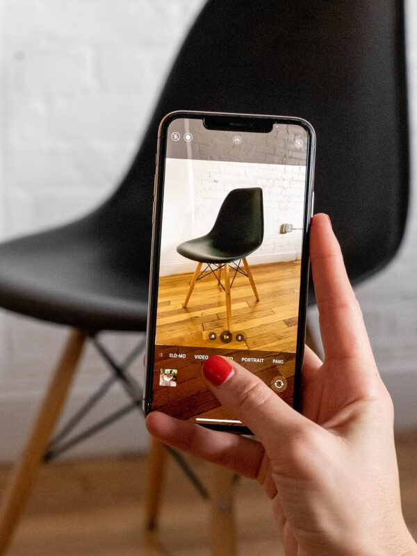 A close up of a phone taking a photo of a black chair. By Kaiyo. 