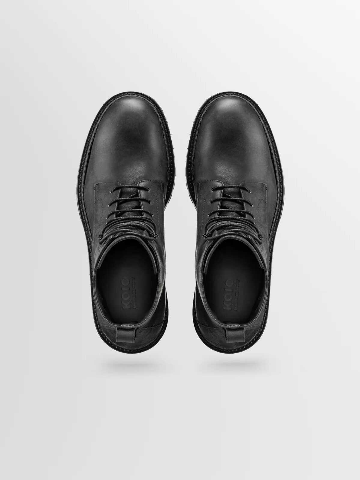 A pair of black Koio boots in front of a light grey background.