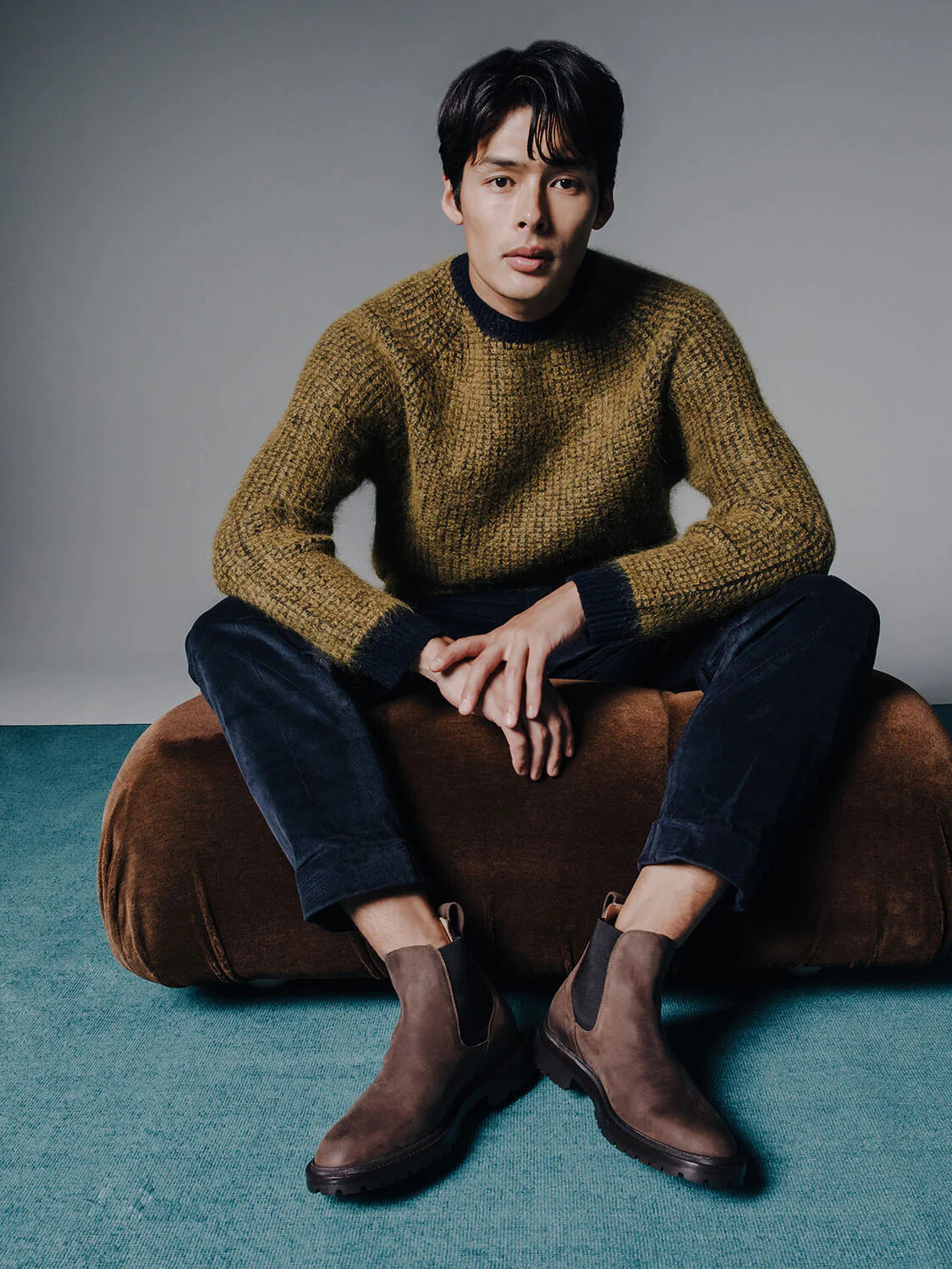 A model seated on a brown cushion wearing Koio brown boots.