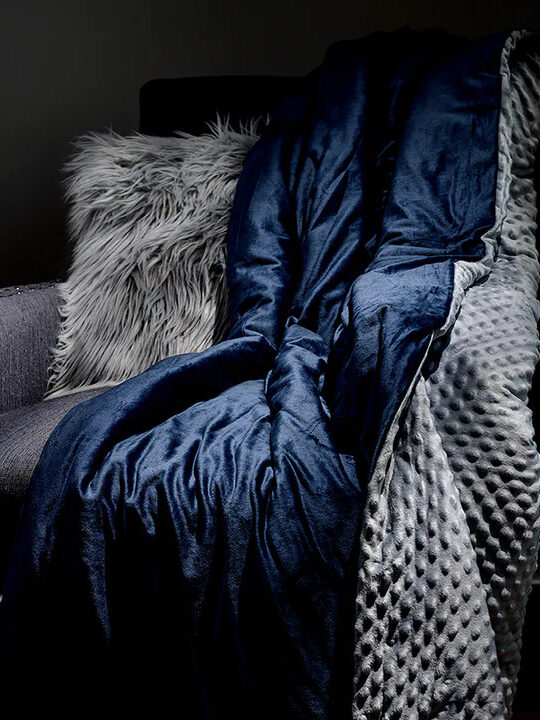 A blue Luxome weighted blanket thrown on a grey sofa.