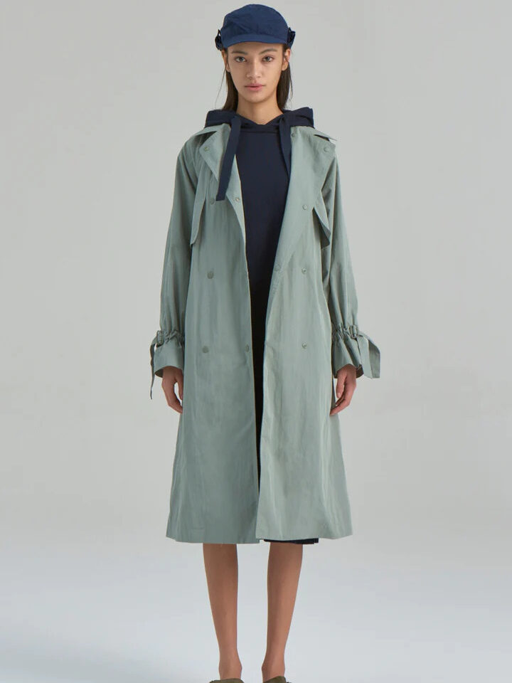 A model wearing a long teal waterproof trench coat by Nau.