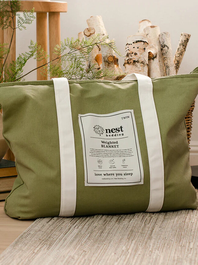 A green Nest Bedding Weighted Blanket tote set on the floor. 