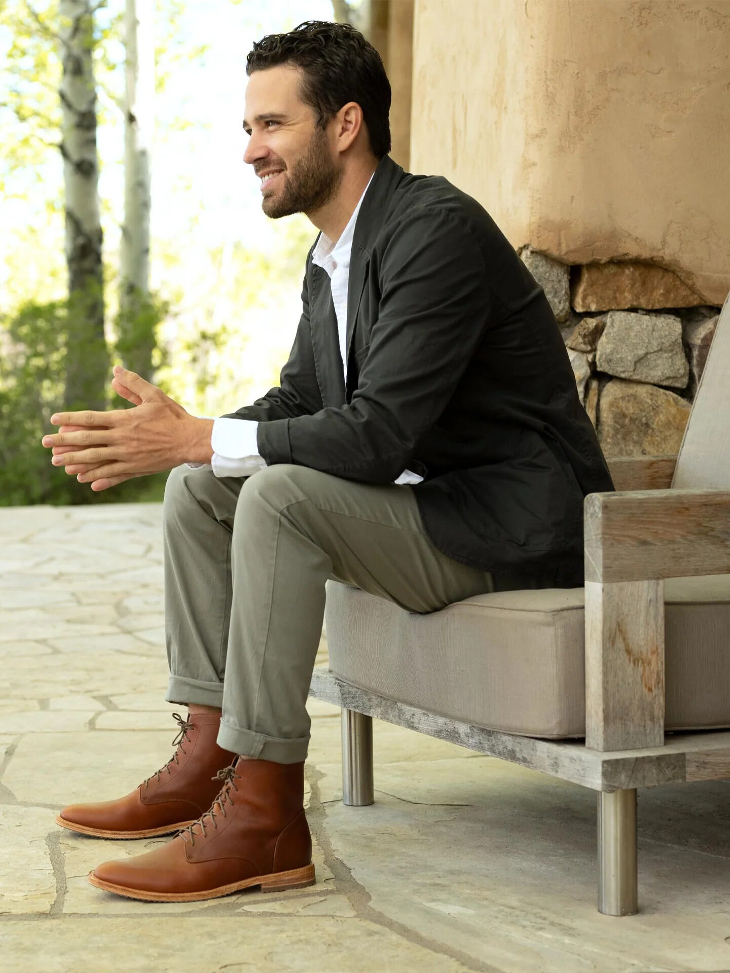 A model sitting on an outdoor chair wearing brown Nisolo boots.