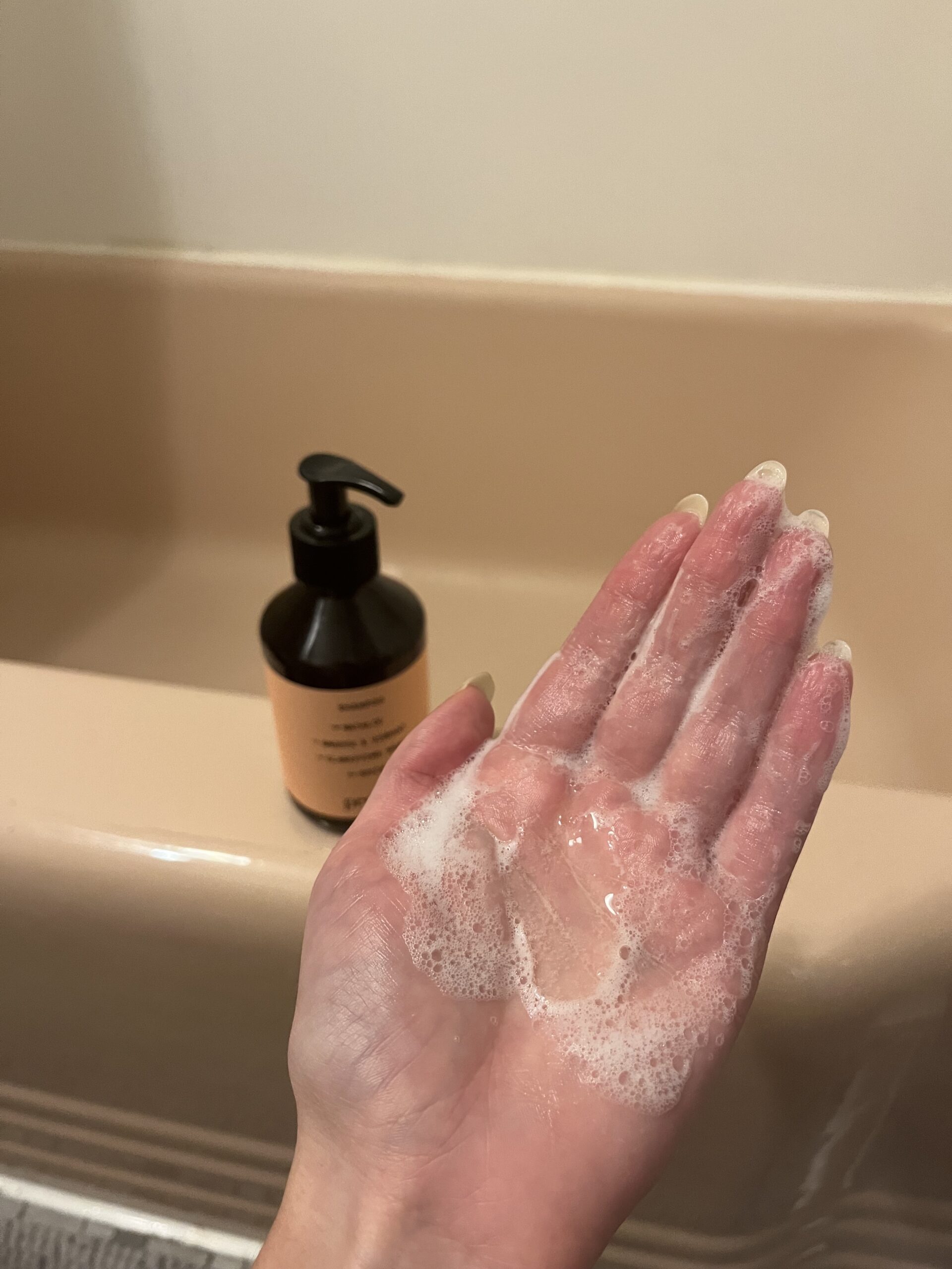 A hand covered in suds next to a bottle of Prose
