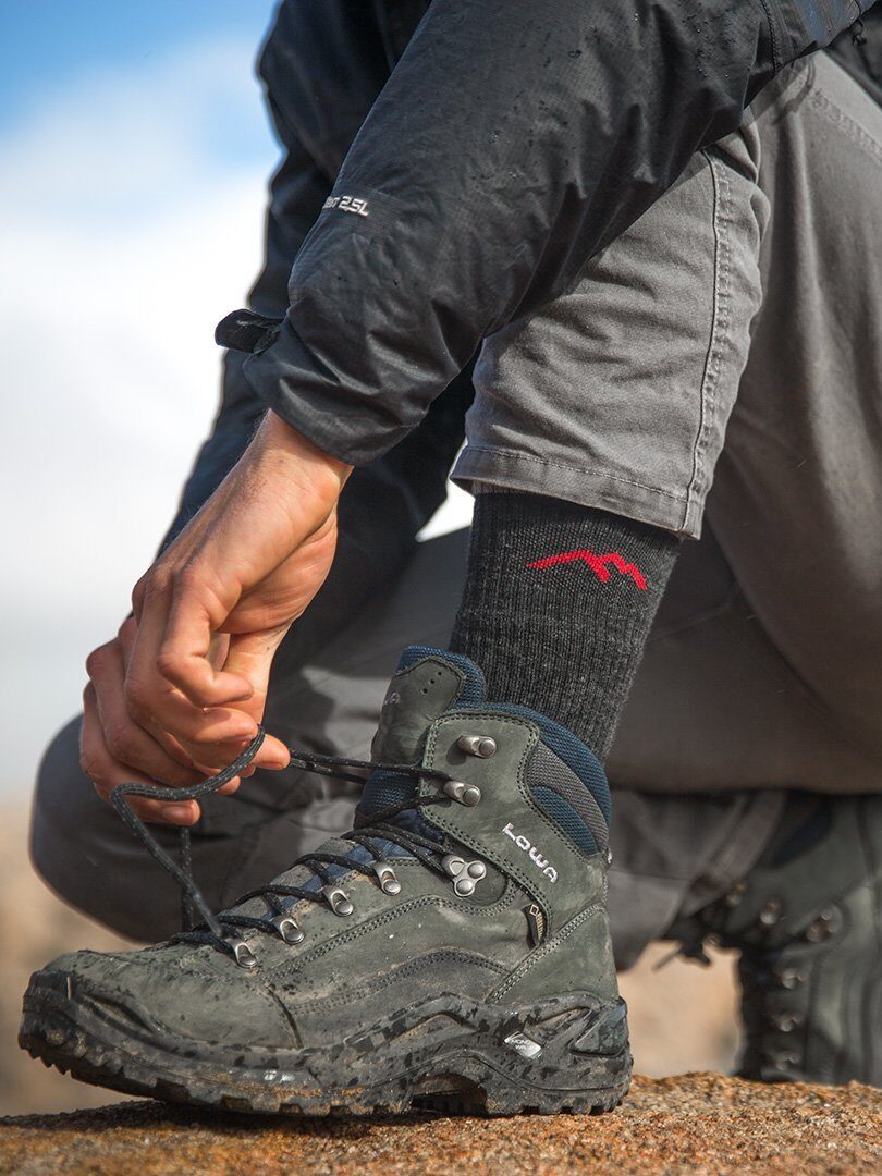 A close up of a model tying up a pair of black Lowa boots.