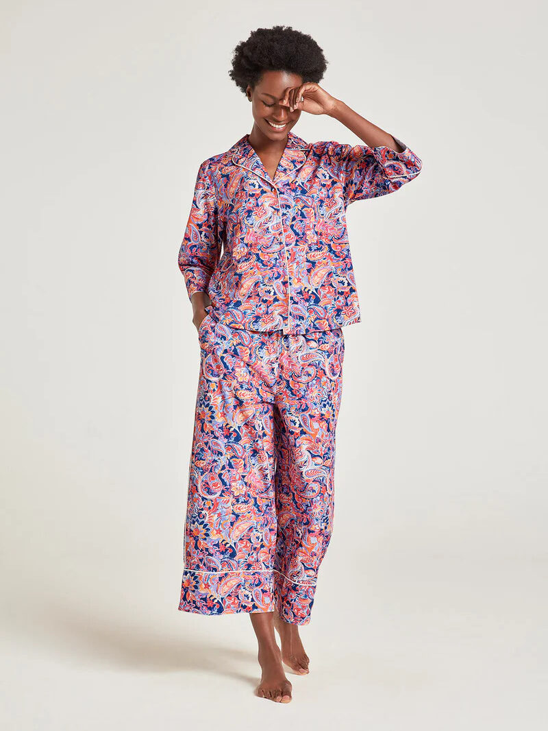 A model wearing a matching pink and blue intricate swirl pattern collared pajama set by Thought.