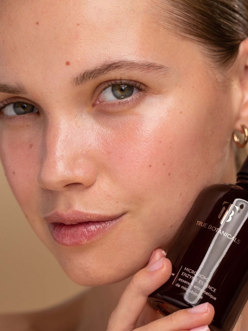 A close up of a woman holding a bottle of True Botanicals Microbiome Enzyme Essence.