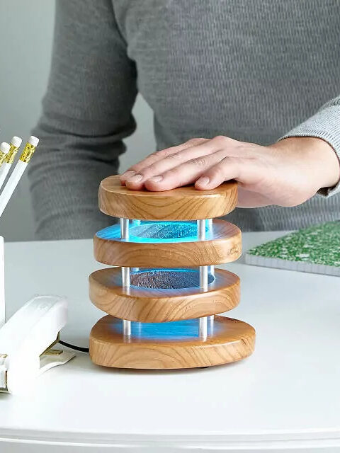 A wooden tiered lamp with blue light between each tier. A hand rests on the top of the lamp. 