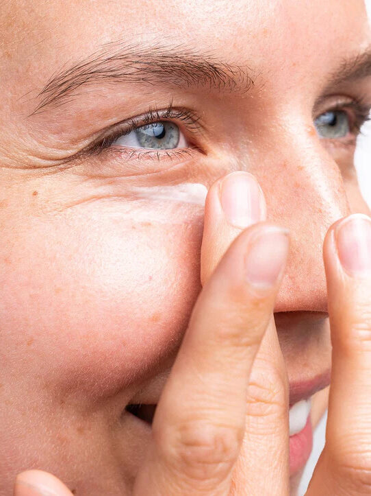 A close up of a woman applying Ursa Major's eye cream to her under eye region. 