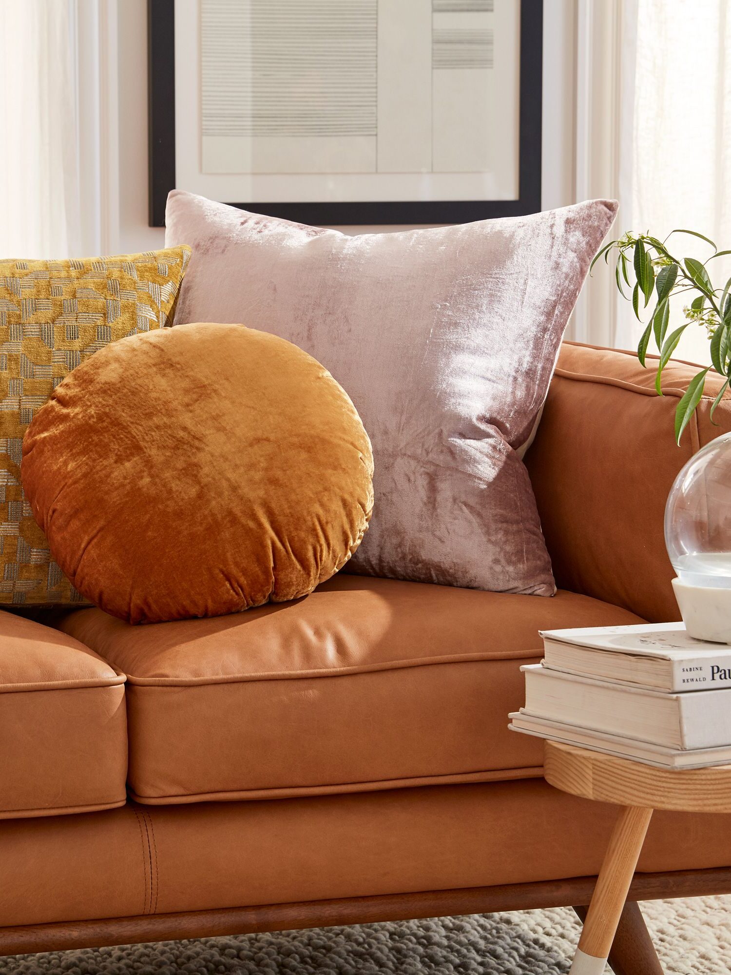 A circular orange decorative velvet pillow and a rectangular pink velvet pillow next to each other on a salmon pink couch by West Elm.