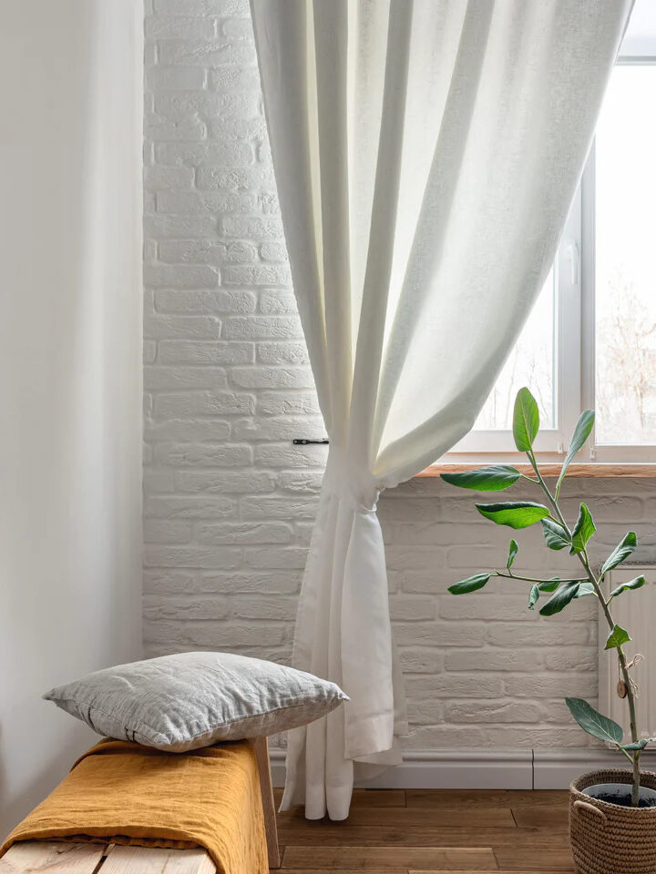 3H linen sheer white curtains gathered at the corner of a window in a room.
