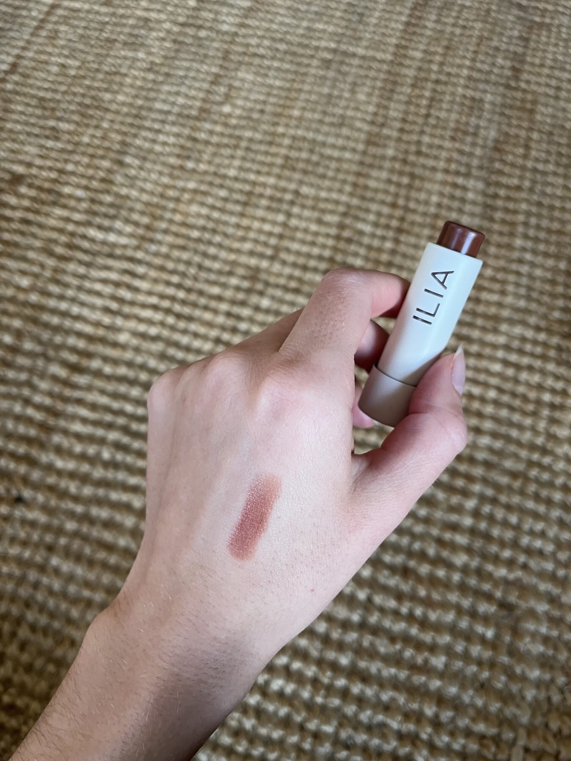 A hand holding Ilia Lip Balm