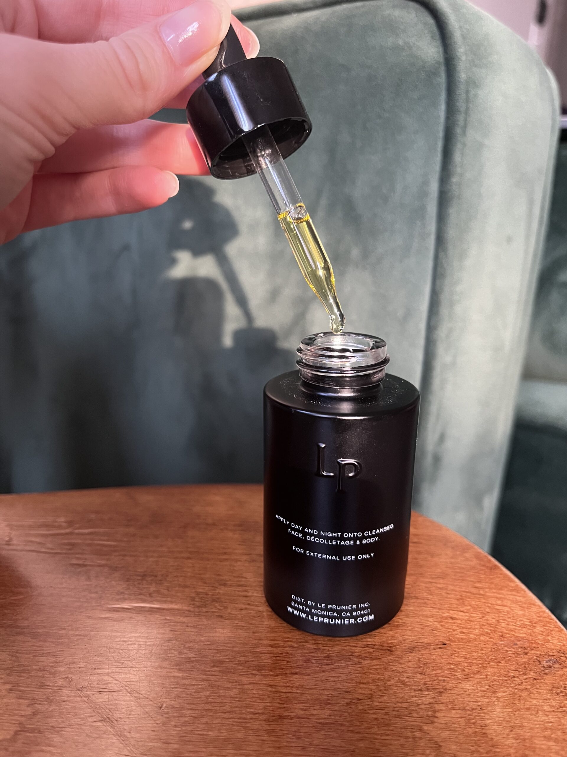 A hand holding the dropper of Le Prunier Beauty Oil