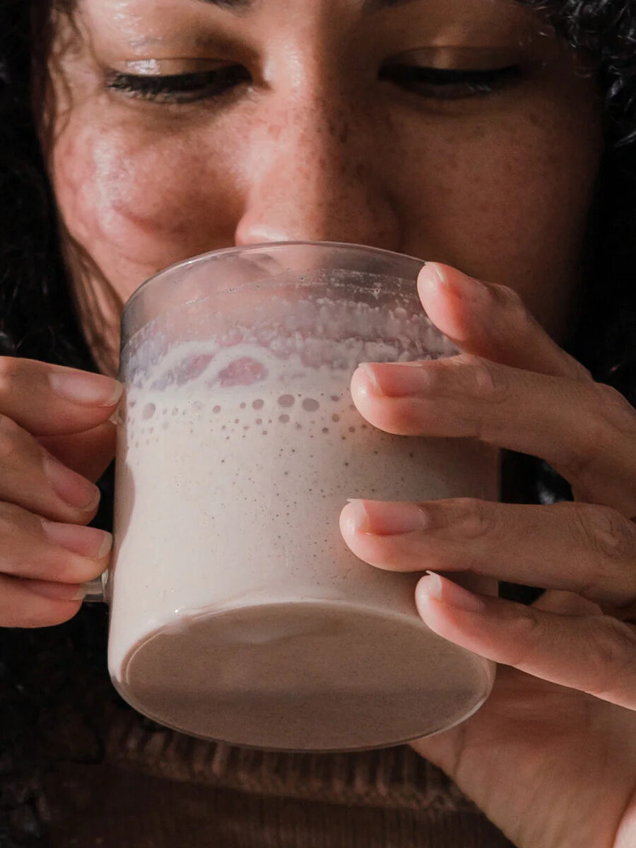 A close up of a model drinking a cup of beam Dream hot cocoa.