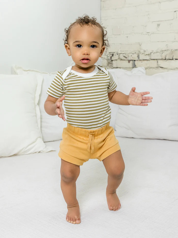 A baby wearing a white and green striped Colored Organics t-shirt and yellow Colored Organics shorts.