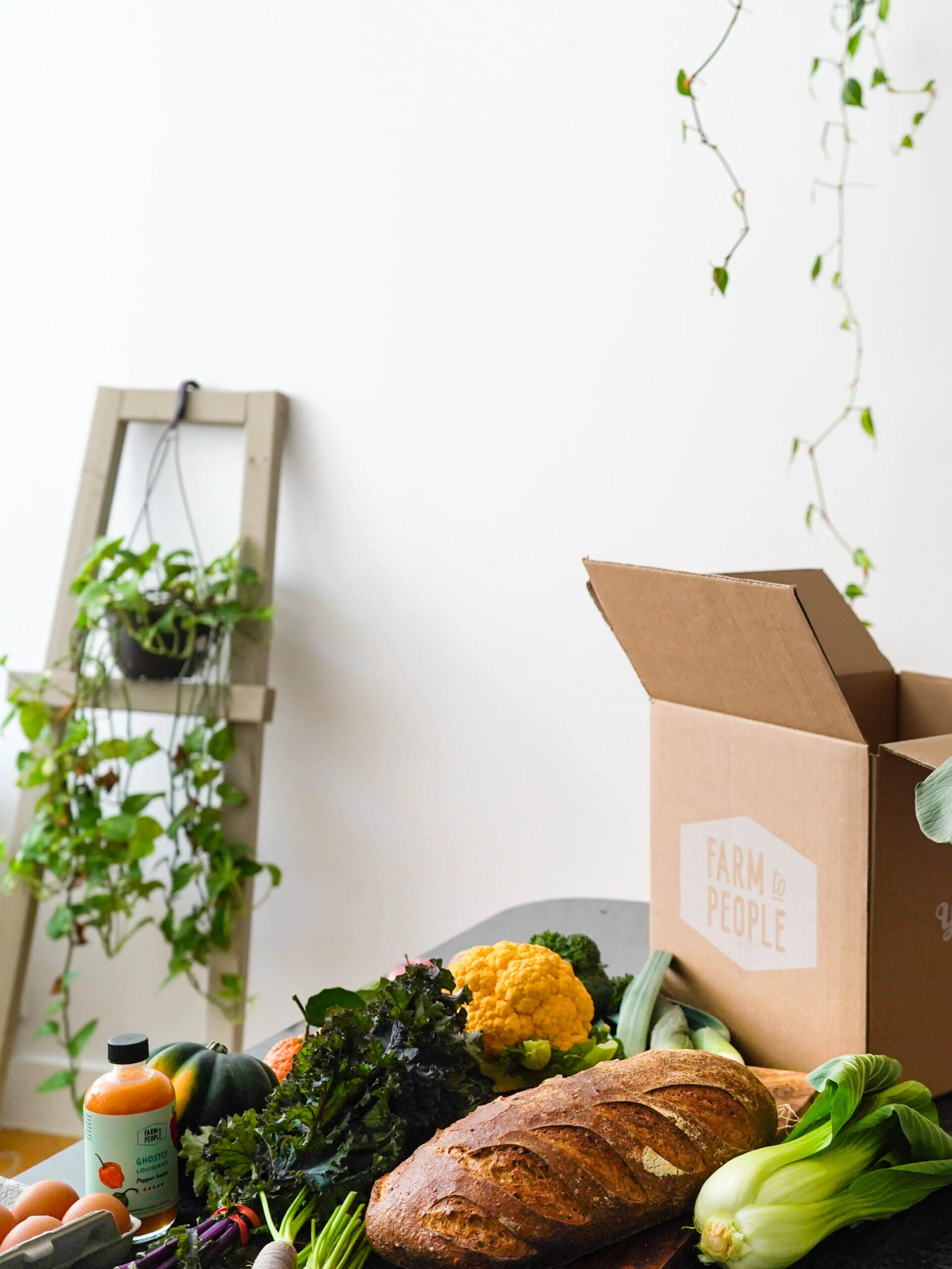 An open Farm To People box, set on a table covered with produce and a loaf of bread.