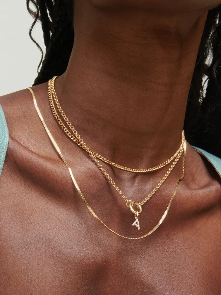 A close up studio shot of a model wearing 3 gold Mejuri necklaces in a layered fashion.