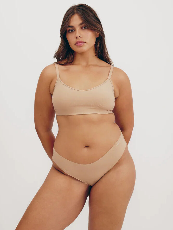 Studio shot of a model wearing a matching Organic Basics nude bralette and underwear set.