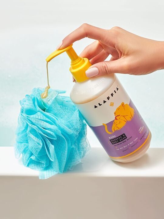 A hand pressing down on the pump of an Alaffia kids shampoo and body wash.