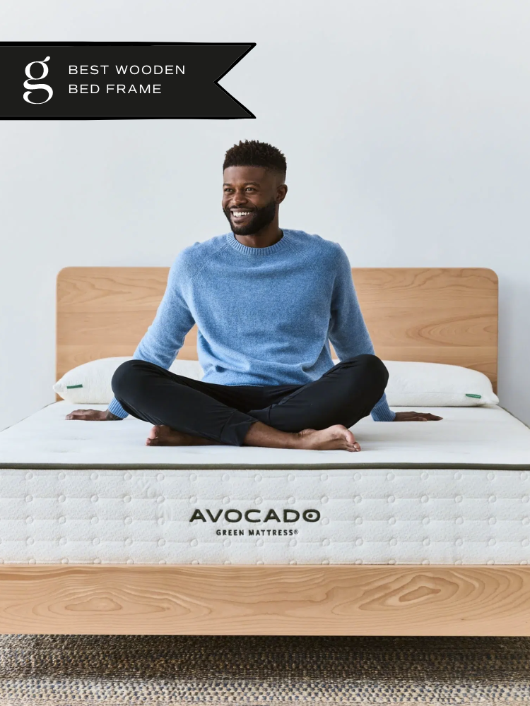 A model sitting cross-legged on an Avocado wooden bed frame.