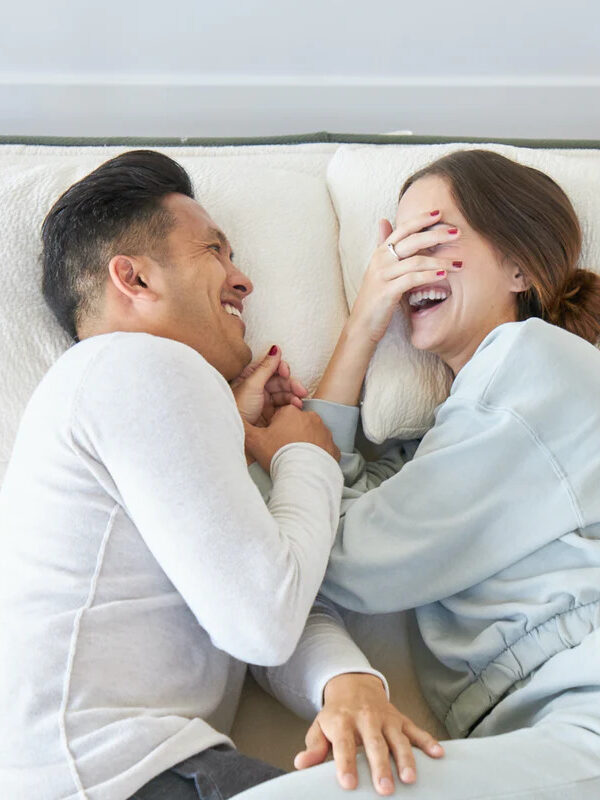 A couple laying down, facing each other on an Avocado mattress.