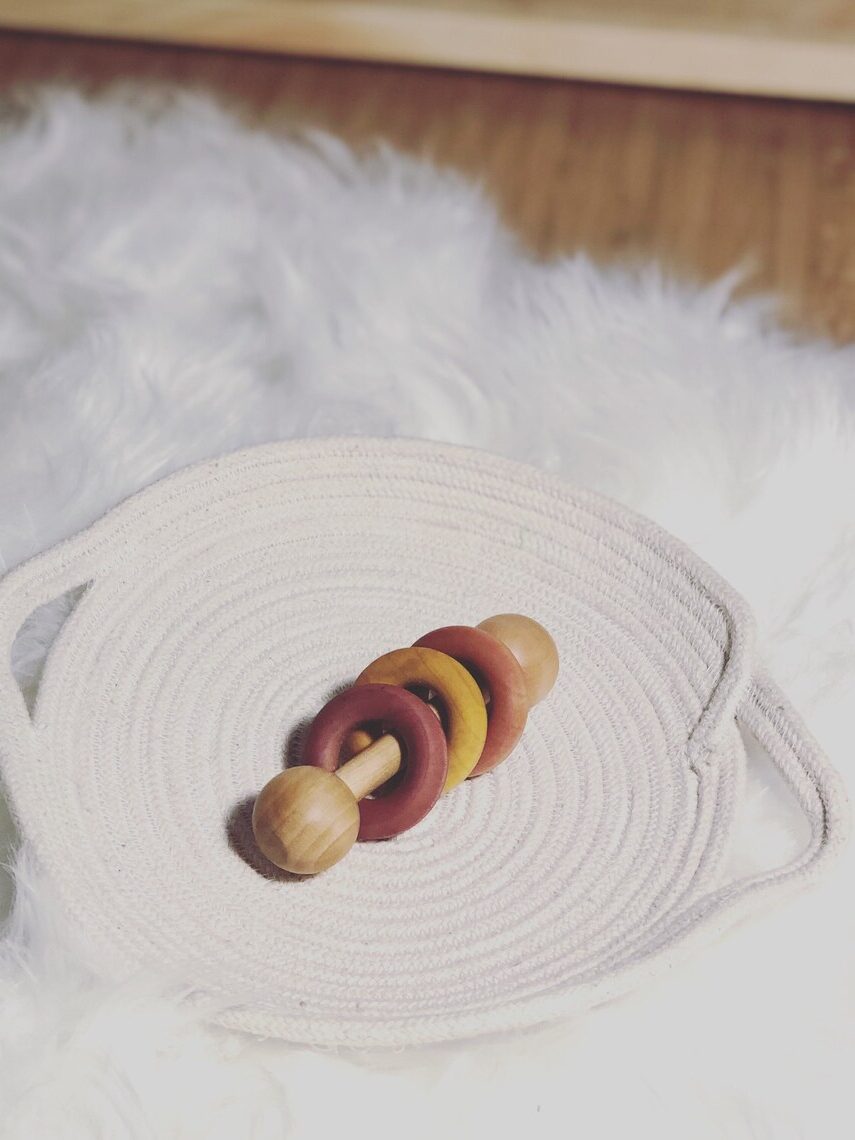 An Essential Montessori wooden rattle on a woven white placemat.