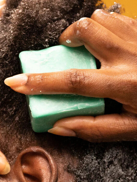 Close up shot of a model applying Ethique's conditioner bar to their hair.