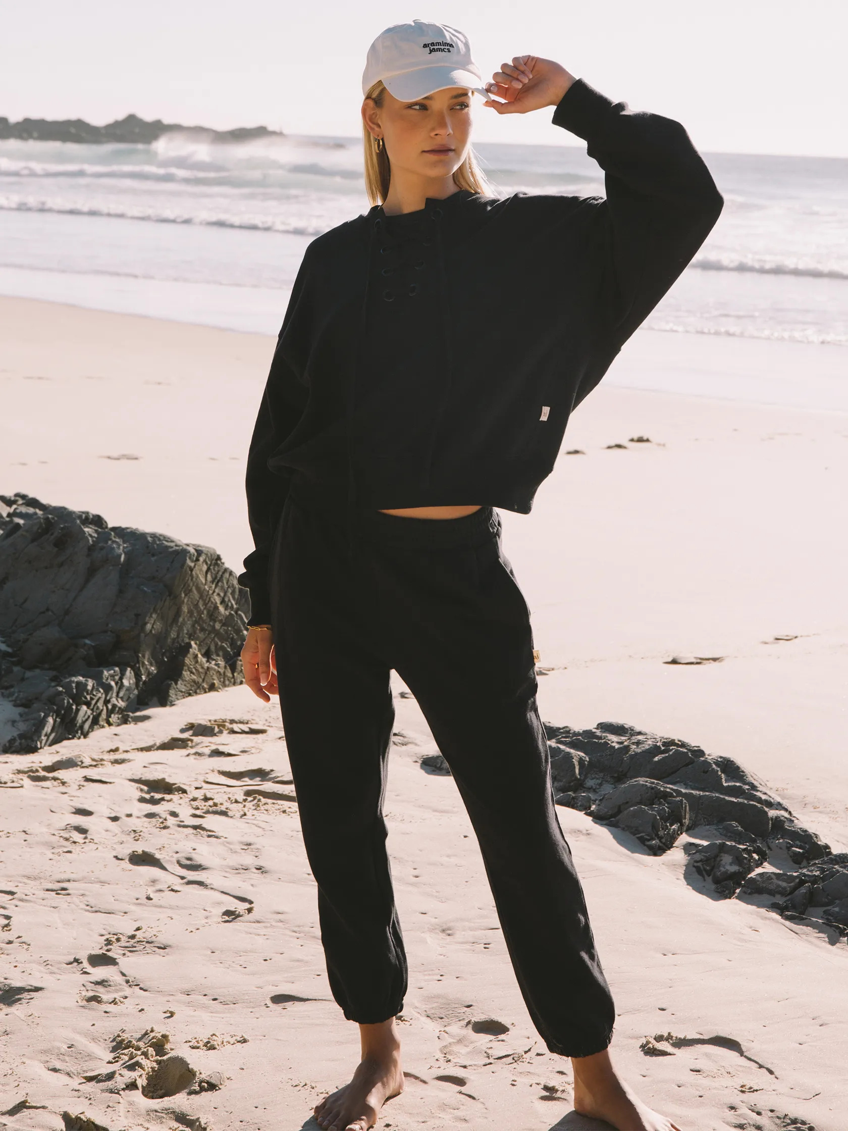 A model on the beach wearing a matching black crewneck sweat set from FashionPass.