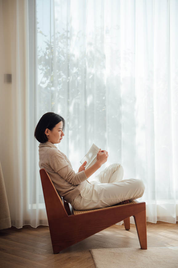 Young Asian beautiful woman reading books on sofa beside the window
