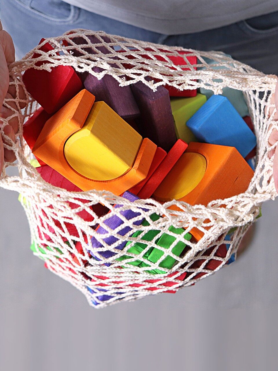 A white mesh bag of Grimm's Montessori colorful blocks.