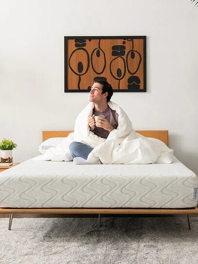 A model wrapped in a white comforter, sitting on a Nest Bedding mattress.