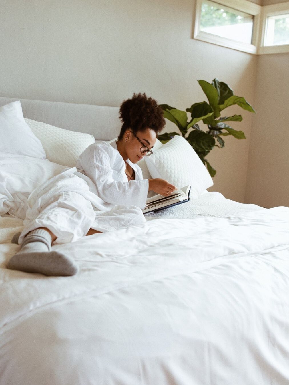 A model in a white robe laying on a Nolah mattress reading a book.