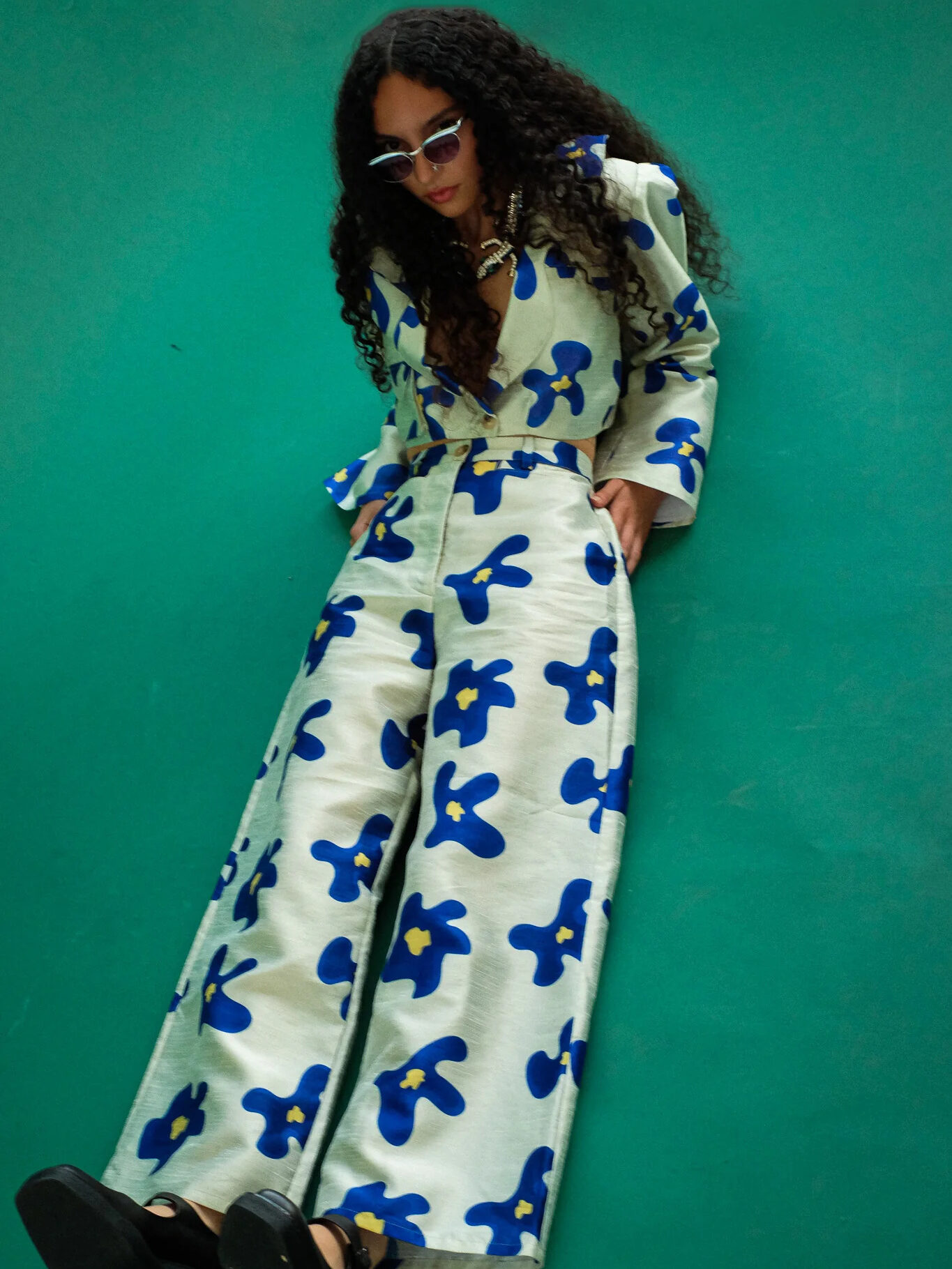 A model, laying seated wearing Selva Negra's matching coco jacket and migo pants in white with blue flowers.