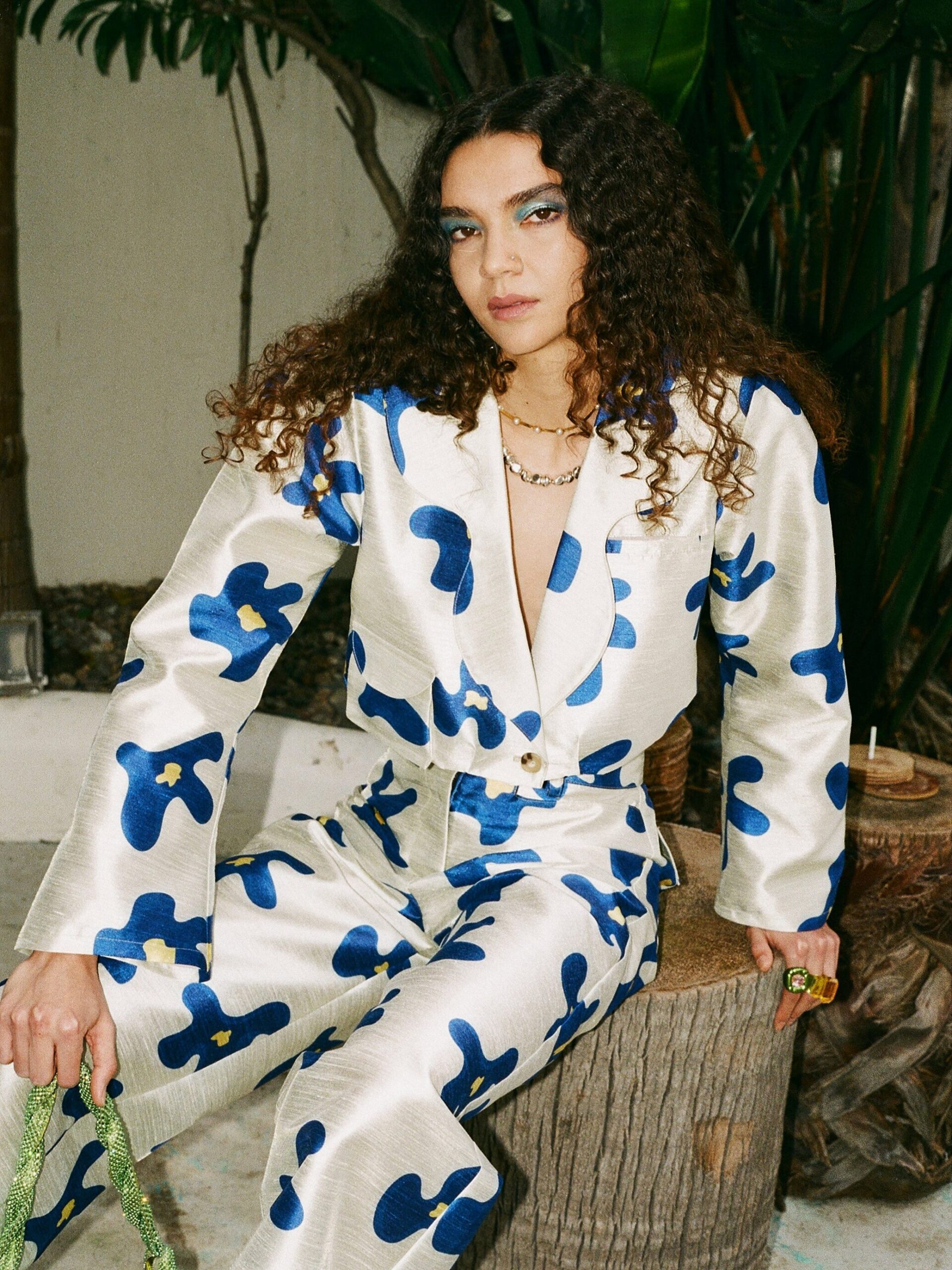 A model, seated wearing Selva Negra's matching coco jacket and migo pants in white with blue flowers.