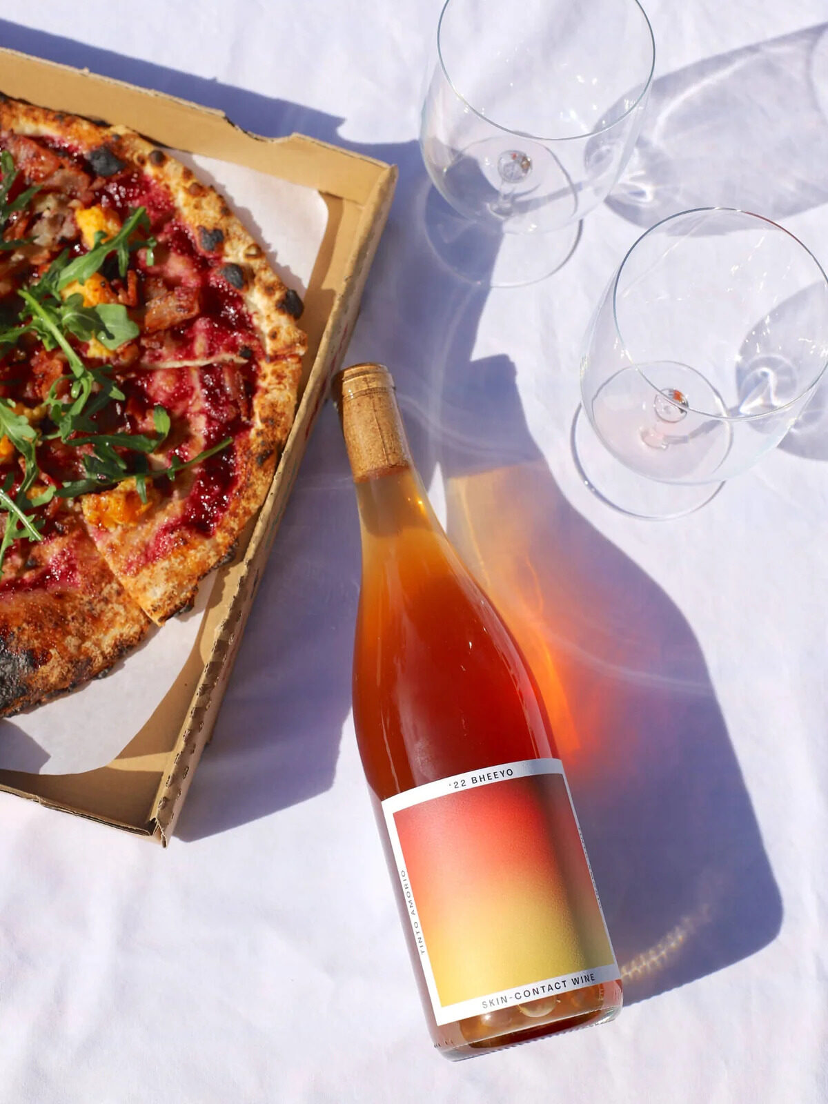 A bottle of Tinto wine on a blanket next to a pizza.