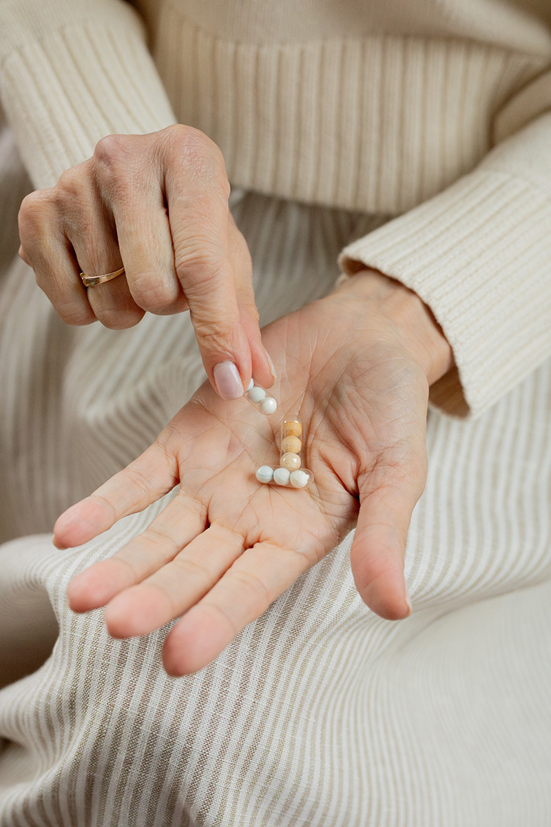 A close-up of an elderly woman's hands holding various pills, with one hand selecting a capsule.