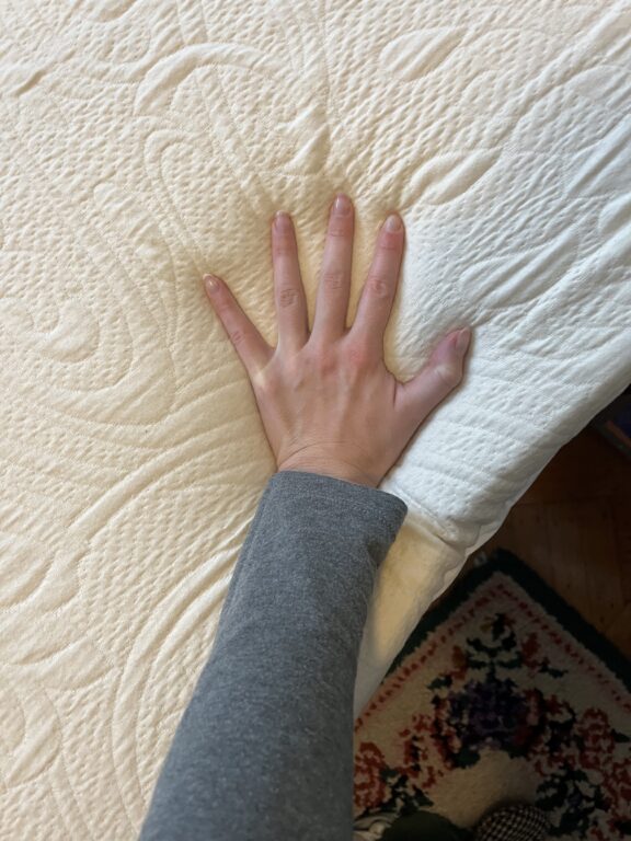 Editor's hand pressing down to test the firmness of the Happsy mattress topper.