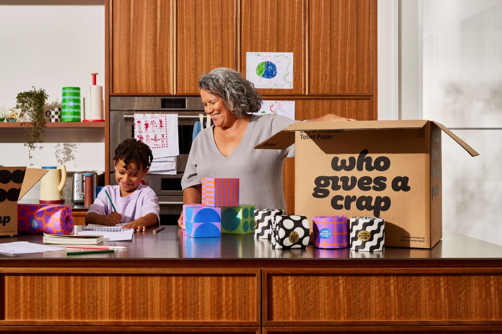 Smiling woman and child unpack toilet paper from a Who Gives A Crap cardboard box