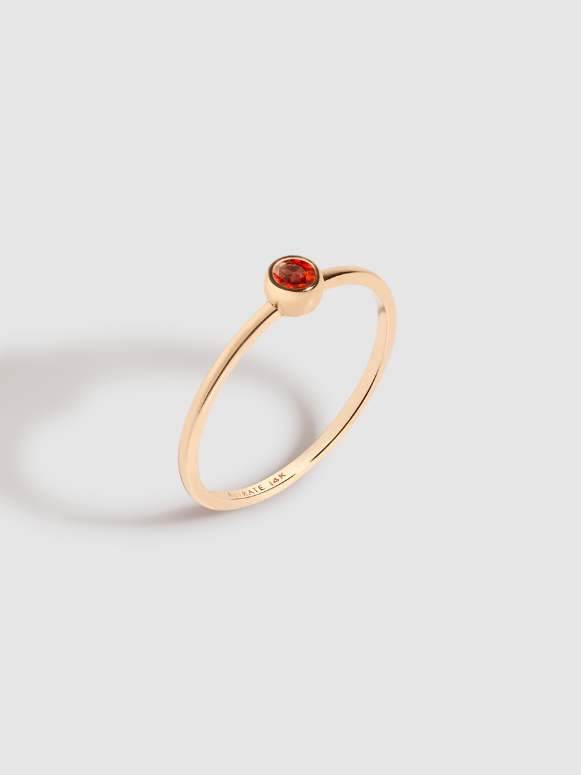 A solitaire gold ring with a small red garnet stone in the center. From Aurate. 