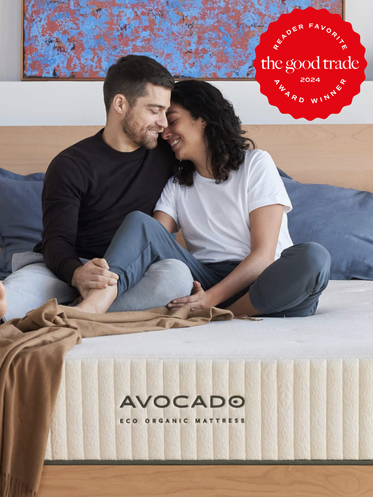 A couple leans into one another while both seated on an Avocado Eco Organic Mattress. The TGT 2024 Award Winner Badge is on the right corner of the image. 